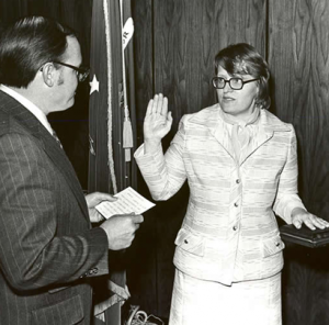 Image description: A black-and-white photo of Carin Clauss with her right hand raised, presumably being sworn in to the United States Department of Labor as a solicitor.