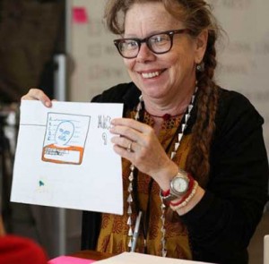 Image description: A photo of Lynda Barry holding up a drawing.