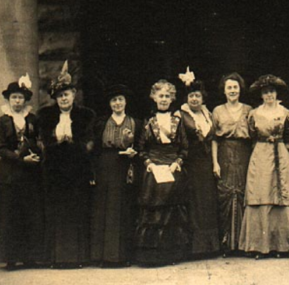 Image description: A black-and-white photo of twentieth century suffragettes standing shoulder-to-shoulder.