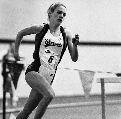 Image description: A black-and-white photo of Suzy Favor Hamilton wearing a Wisconsin uniform while running at a track event.