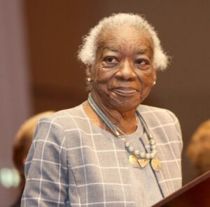 Image description: A photo of Milele Chikasa Anana standing at a podium.